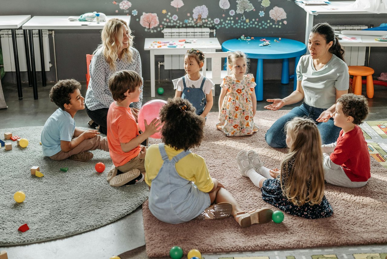 Kindergartenkinder mit Erzieherinnen im Spielkreis